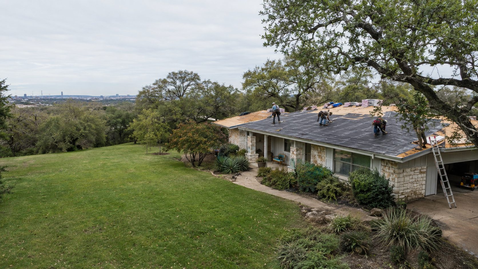 A wide drone shot of a crew re-roofing the home at a 1950s Austin ranch house with limestone accents and live oaks in Austin, TX